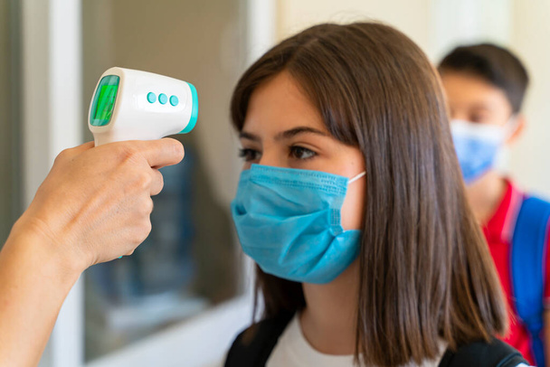 Teacher checking temperature of students with face mask for pandemic while children go back to school - Photo, image