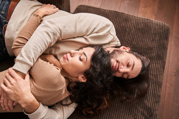 Loving couple laying on sofa indoors at home and hugging - 写真・画像
