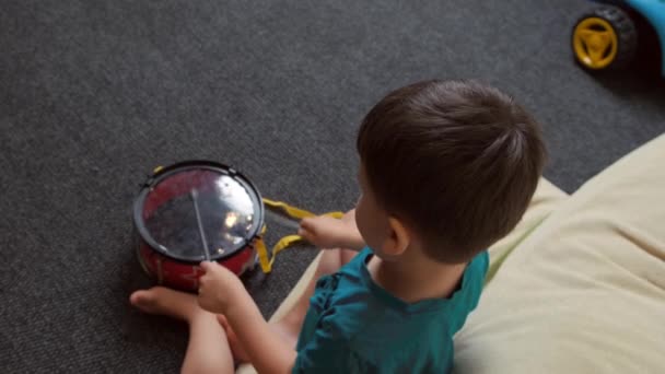 Boy sitting on floor and playing with plastic toy drum. Top view. - Metraje, vídeo