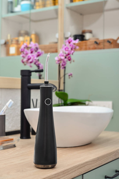 Schwarzer tragbarer oraler Bewässerungsapparat auf heller Holzarbeitsplatte in moderner Badezimmer-Nahaufnahme - Foto, Bild