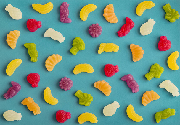 Jelly candies in shape of fruits, trees and birds as pattern on blue background - Φωτογραφία, εικόνα