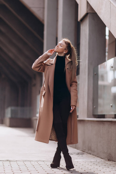 A young beautiful girl in a beige coat stands on the street. clothing advertisement - Foto, Imagen