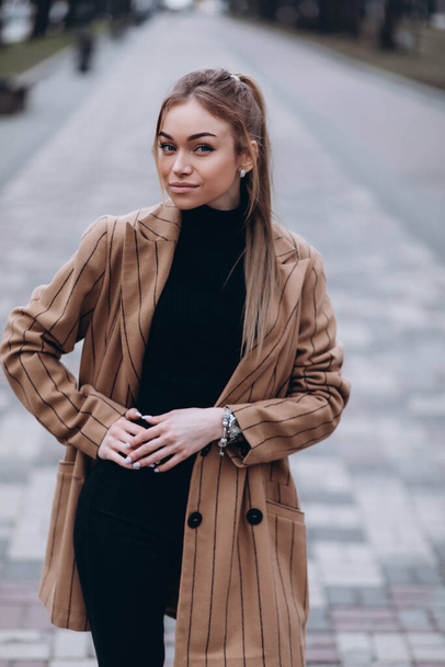 Young beautiful girl in a beige jacket posing on the streets of the city. clothing advertisement - Foto, afbeelding