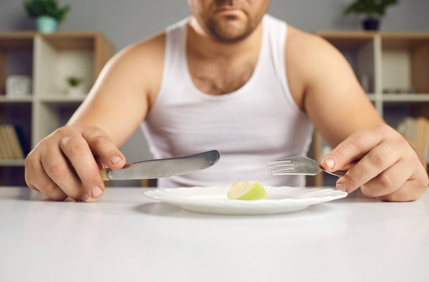 Cropped view sad man on diet holding cutlery near plate with small apple piece - Foto, Imagem
