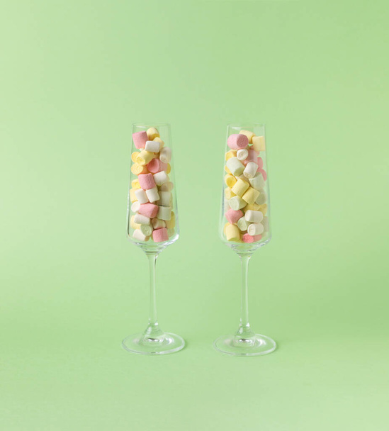 Two tall glass glasses filled with colorful marshmallows on a green background. The concept of happiness and success. - Zdjęcie, obraz