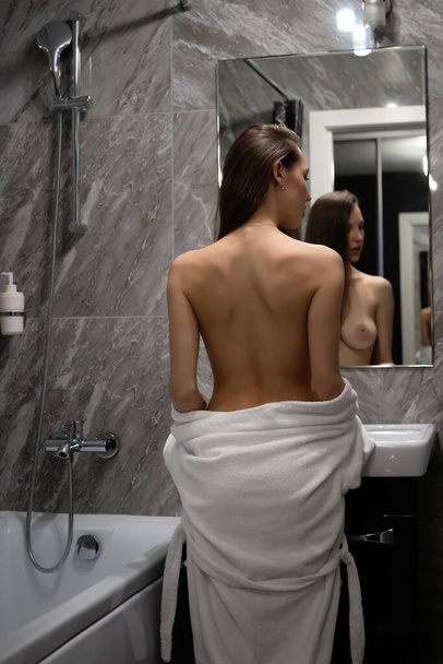 Vista posteriore di graziosa femmina sexy con seno nudo in piedi davanti sullo specchio in bagno - Foto, immagini