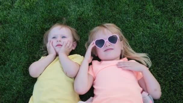 Happy little sisters lies on green grass. Older Sister Kisses her Little Sister. - Filmagem, Vídeo