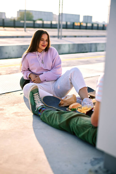 Teenagers sitting outdoors and having fast food for a snack. Urban teenagers hanging out after school. - Foto, Imagem