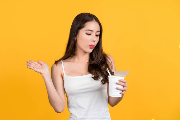 Asian beautiful woman eating spicy instant noodles on yellow background she is enjoying eating - Fotó, kép