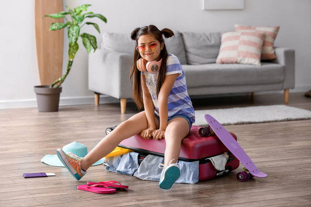Cute little girl trying to pack suitcase at home - Foto, afbeelding