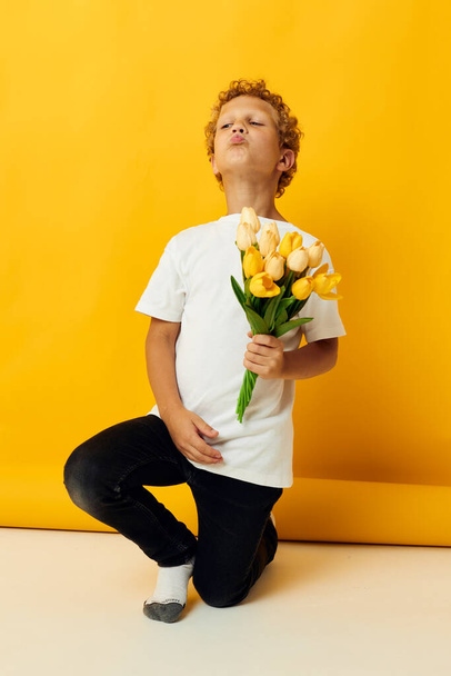 Little boy holding a bouquet of flowers a gift yellow background unaltered - Fotografie, Obrázek