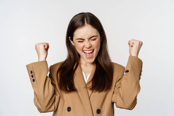 Enthusiastic girl screaming and rejoicing, looking at camera, winning, celebrating victory and triumphing, standing over white background - Foto, imagen