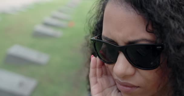 Muotokuva surullisesta mustasta naisesta aurinkolaseissa seisomassa hautausmaalla. Hautajaiset ja jäähyväiset, kunnioittaen läpäisseet sukulaiset. 4k 60p Prores - Materiaali, video