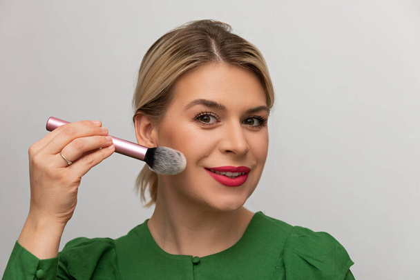 Young beautiful woman applying her make-up with a brush - Foto, Imagen