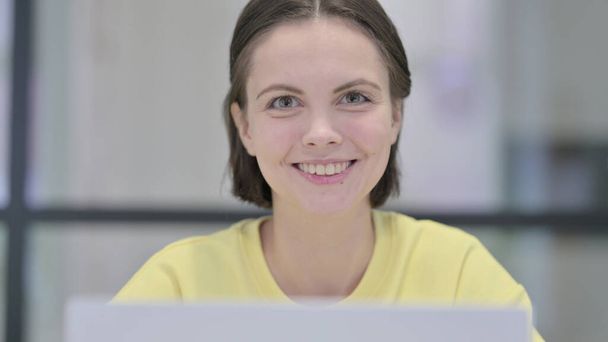 Primer plano de la mujer con el ordenador portátil sonriendo en la cámara - Foto, imagen