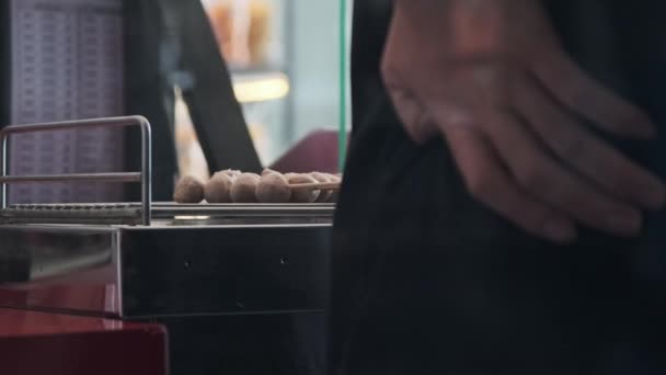 Mão de um comerciante que brinda almôndegas em espetos em um fogão elétrico. Comida de rua em Tailândia. - Filmagem, Vídeo