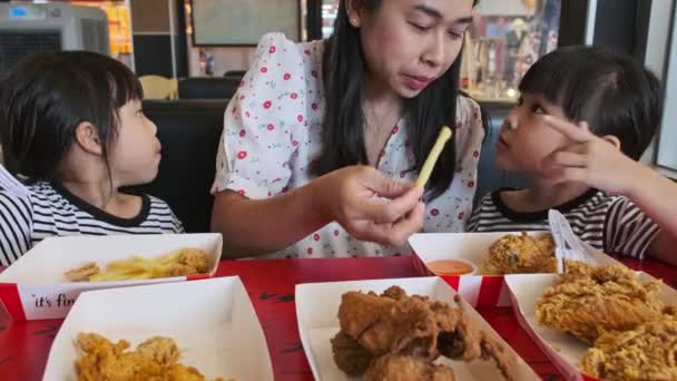 Schattige kleine Aziatische meisjes eten gebakken kip en frietjes samen met een mooie moeder in een fast food restaurant. - Video