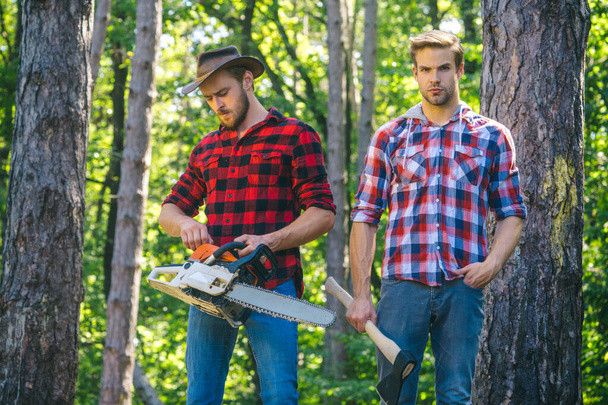 Woodcutters with chainsaw lumberjacks with axe. Hipsters men on serious face with axe. Lumberjack brutal and bearded holds axe. Two lumberjacks in forest - Photo, image