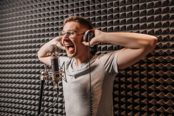 The vocalist sings in the studio in a microphone. Man in headphones writes a podcast, an audiobook. Artist, recording an album, working with the label. Announcer records a speech at a radio station - Foto, afbeelding