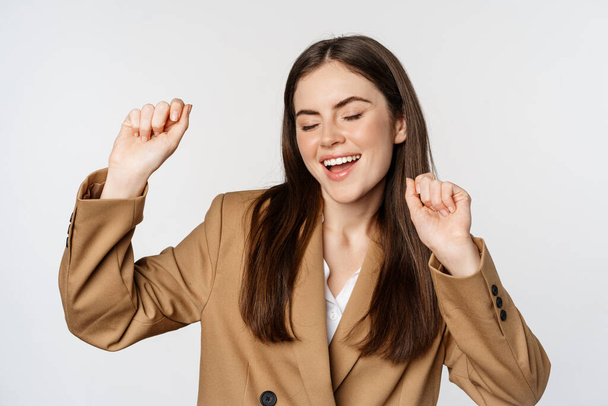 Successful businesswoman, saleswoman dancing and having fun, wearing office suit, posing over white background - Fotoğraf, Görsel