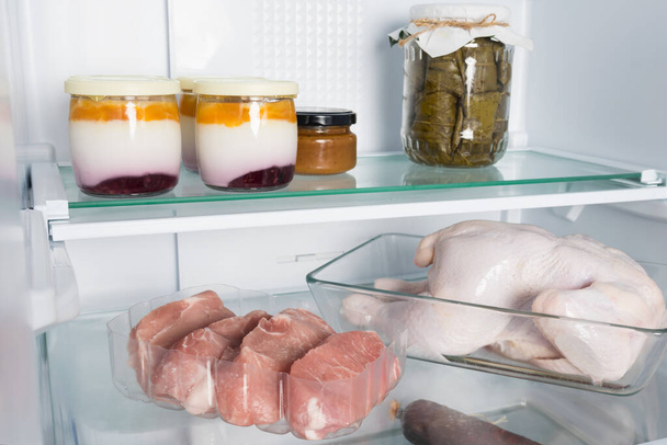 meat and dairy products are on a shelf in an open refrigerator - Photo, Image