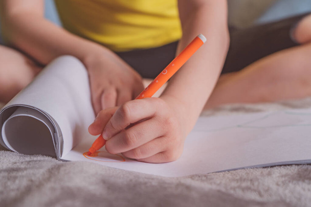 Молодий білий хлопчик малює в альбомі, пише на папері вдома, сидячи на ліжку
. - Фото, зображення