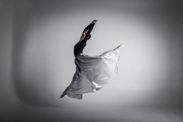 ballerina. A young elegant ballet dancer, dressed in professional attire, shoes and a blue weightless skirt, demonstrates her dancing skills. The beauty of classical ballet. Black and white photo - Foto, Imagen