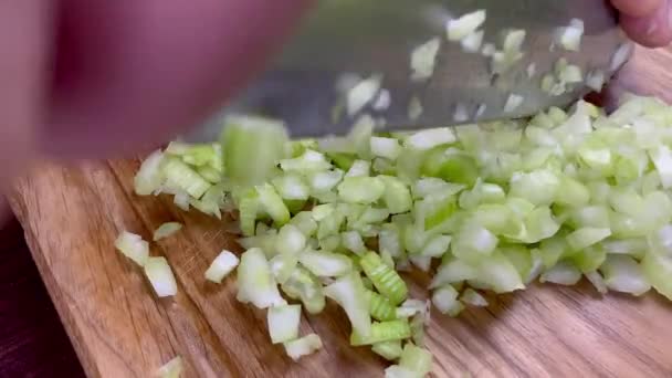 Chef hands chop finely raw celery stalk on wooden cutting board with kitchen knife. Slow motion. - Filmati, video
