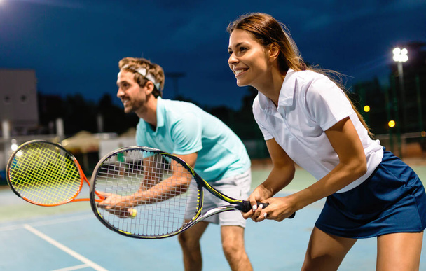 Beautiful young couple are playing tennis as a team on tennis court outdoors. People sport concept - Valokuva, kuva