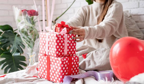 Valentine's day, Women's day. Young caucasian brunette woman sitting in the bed celebrating valentine day wrapping the gifts - Foto, Imagen