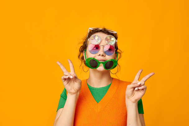 portrait of a young woman multicolored sunglasses on face posing grimace yellow background unaltered - Photo, Image