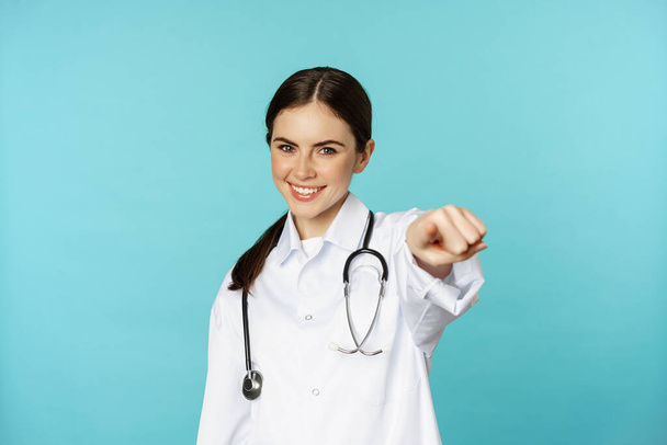 Young professional woman doctor, medical worker showing okay, ok zero gesture and smiling satisfied, recommending, complimenting smth, torquoise background - Φωτογραφία, εικόνα