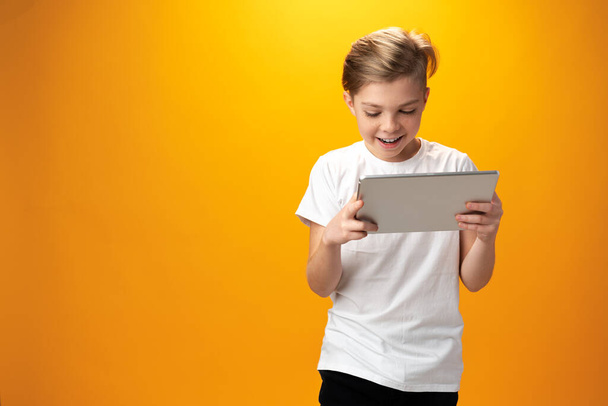 Little boy playing with digital tablet against yellow background - Foto, Imagen