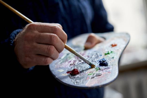 Closeup view of artist painting with palette, brush and acrylic colour paints in art studio indoors - Valokuva, kuva