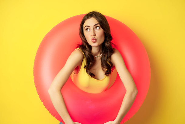 Close up portrait of coquettish young sexy woman inside pink swimming ring, concept of beach holiday, vacation and summer, yellow background - Photo, image