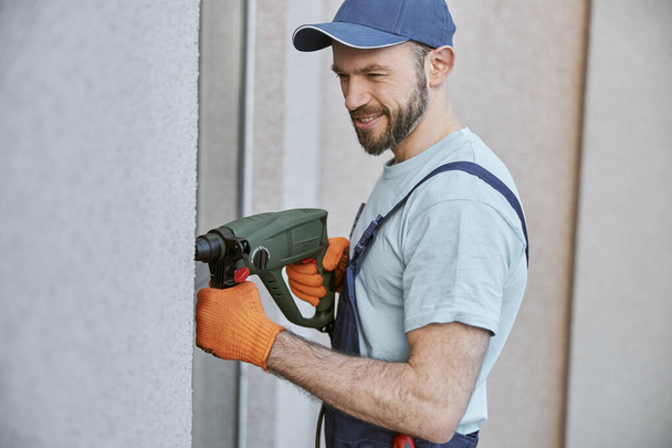 Joyful young man drilling wall with hammer drill - Фото, изображение