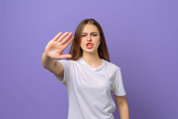 Displeased student girl saying NO, showing rejection gesture, frustrated screaming, wears blank white t shirt, standing over purple background. Concept of warning, prohibitionr - Foto, afbeelding