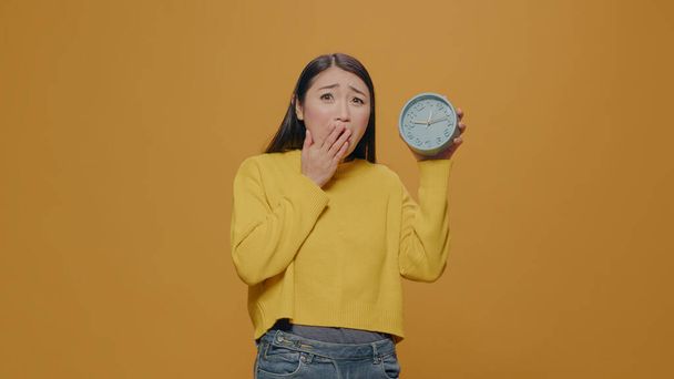 Asian woman with anxiety checking time on clock in studio - Φωτογραφία, εικόνα