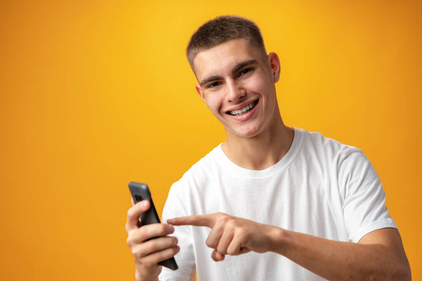 Young casual man teenager using a smartphone against yellow background - Fotografie, Obrázek