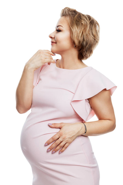 Beautiful pregnant woman. Smiling blonde in a pink dress. Happy motherhood, love and tenderness. Profile view. Isolated on white background. Vertical. - Photo, image