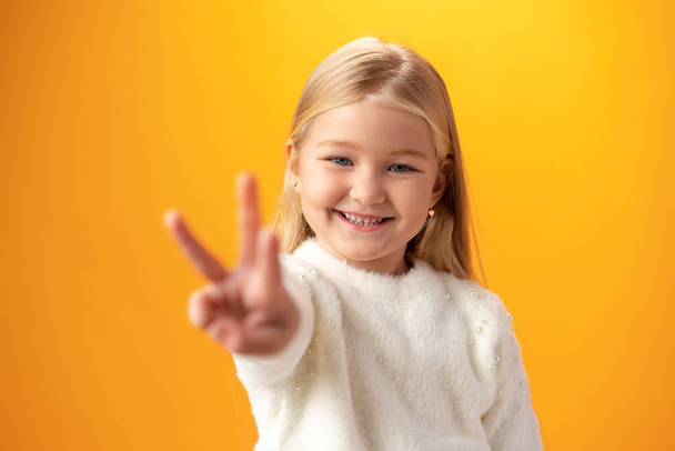 Little girl showing and pointing up with fingers number three against yellow background - Фото, зображення