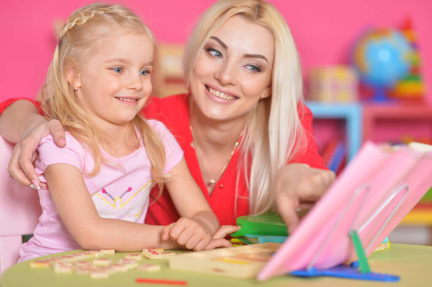 little cute girl  with mother studying at the table at home - Foto, Imagen