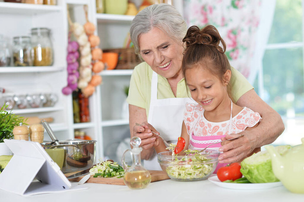 Portrait of happy senior woman with her little grand daughter at kitchen - Фото, изображение
