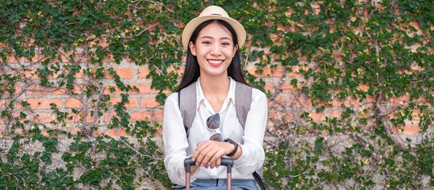 Smiling woman traveller sitting holding dragging black suitcase luggage while walking to passenger boarding in airport, Travel concept. - Photo, Image