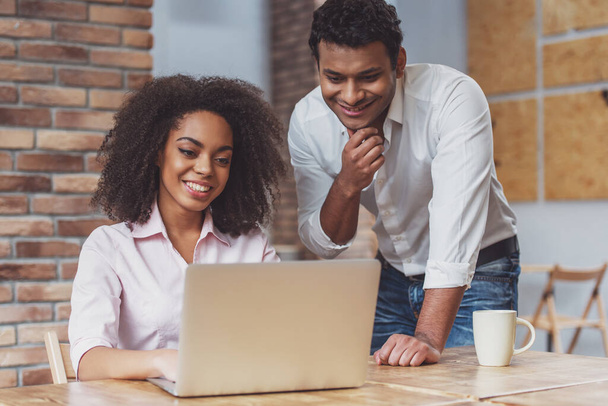 Giovane attraente coppia d'affari afro-americana utilizzando il computer portatile, parlando e sorridendo mentre si lavora in un caffè
 - Foto, immagini