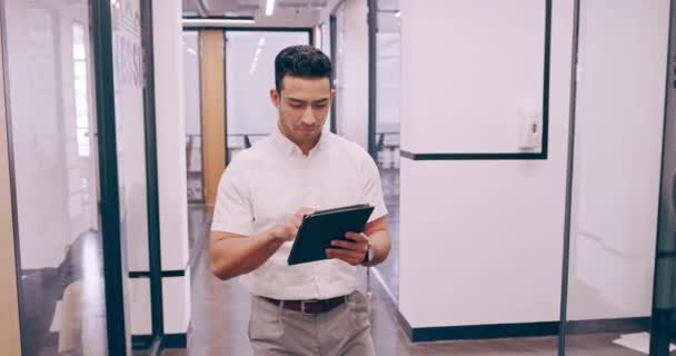 4k video footage of a young businessman working on a tablet and checking the time on his wrist watch as he walks through his office - Imágenes, Vídeo