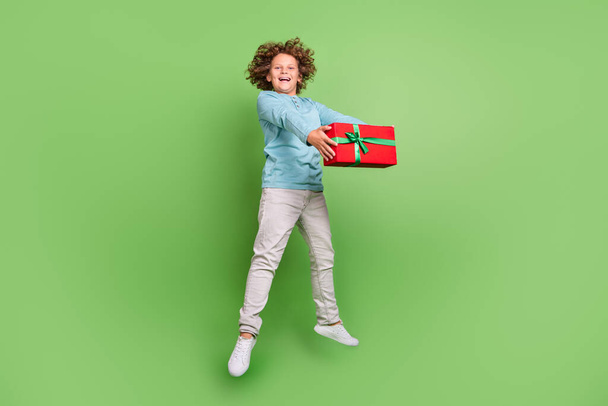 Full length body size view of attractive cheery trendy guy jumping giving giftbox isolated over bright green color background. - Foto, afbeelding