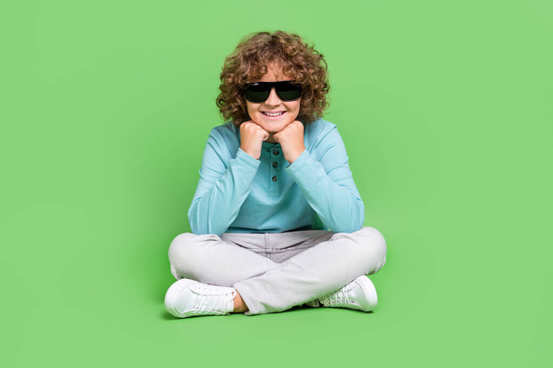 Retrato de chico alegre atractivo sentado descansando usando especificaciones aisladas sobre fondo de color verde vivo. - Foto, imagen