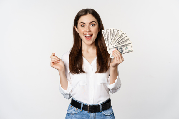 Захоплена жінка, показуючи гроші, готівку і посміхаючись, отримала кредит, мікрокредит, стоячи в захваті на білому тлі
 - Фото, зображення