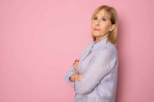 Senior woman posing with arms folded standing isolated over pink background. - Photo, Image